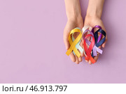 Женские руки с различными атласными лентами на сиреневом фоне, крупный план. Всемирный день борьбы против рака. Стоковое фото, фотограф Pixel_shot / Фотобанк Лори