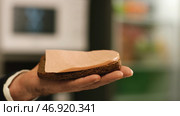 Close-up of man's hand holding a piece of Borodino rye bread with slice of Doctor's sausage falling on it. Стоковое фото, фотограф David Kashakhi / Фотобанк Лори