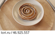 Tasty sweet puff rolls with honey and white glaze lying on the white plate and rotating on the wooden round board. Стоковое фото, фотограф David Kashakhi / Фотобанк Лори