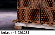 Close up of a pile of stacked clay bricks with holes placed on wooden pallet in dark storage room. Стоковое фото, фотограф David Kashakhi / Фотобанк Лори