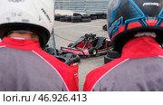 Close up of racer backs wearing special uniforms and helmets going to the kart cars, competition and race concept. Стоковое фото, фотограф David Kashakhi / Фотобанк Лори