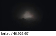 Light passing trough a hole illuminating a mysterious dark cave with a small red signal flare in the fog. Стоковое фото, фотограф David Kashakhi / Фотобанк Лори