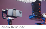 USA - New York, 09.25.2021: close up of new smartphone and camera fixed by stabilizers isolated on a pink wall background. Редакционное фото, фотограф David Kashakhi / Фотобанк Лори