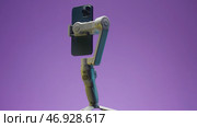 New professional phone with three cameras rotating with stabilizer on lilac wall background. Редакционная иллюстрация, иллюстратор David Kashakhi / Фотобанк Лори
