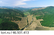 Beautiful view from above of farm fields surrounded by high mountains covered with green trees and shrubs in summer sunny day against blue sky. Стоковое фото, фотограф David Kashakhi / Фотобанк Лори