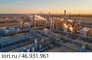 Промышленный пейзаж на рассвете с панорамным видом с беспилотника на нефтеперерабатывающий завод, излучающий золотистый солнечный свет. Стоковое AI-изображение, AI-художник ФотоИнтеллект / Фотобанк Лори