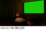 Young girl sitting on sofa against tv with chroma key green screen, back view. Стоковое фото, фотограф David Kashakhi / Фотобанк Лори