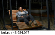 Beautiful woman is swinging on recumbent swing and talking on phone. Стоковое фото, фотограф David Kashakhi / Фотобанк Лори