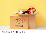 Коробка ненужных вещей и картонный знак с надписью "РАСПРОДАЖА НА ГАРАЖЕ" на желтом фоне. Стоковое фото, фотограф Pixel_shot / Фотобанк Лори