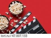 Миски с вкусным попкорном и киношной хлопушкой на красном фоне. Стоковое фото, фотограф Pixel_shot / Фотобанк Лори