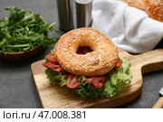 Деревянная доска с вкусным сэндвичем с бубликом, жареным беконом и салатом на черном фоне. Стоковое фото, фотограф Pixel_shot / Фотобанк Лори
