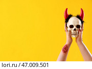 Зомби руки, держащие череп с рожками дьявола на желтом фоне. Празднование Хэллоуина. Стоковое фото, фотограф Pixel_shot / Фотобанк Лори
