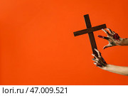 Руки зомби с деревянным крестом на оранжевом фоне. Празднование Хэллоуина. Стоковое фото, фотограф Pixel_shot / Фотобанк Лори