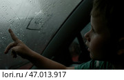 The child draws pictures with his finger on a wet misted window on a cloudy day. Стоковое фото, фотограф David Kashakhi / Фотобанк Лори