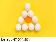 Треугольник из треснутых и целых куриных яиц на желтом фоне. Стоковое фото, фотограф Pixel_shot / Фотобанк Лори