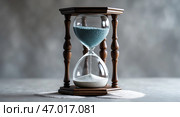 Elegant hourglass filled with blue and white sand resting on a gray surface, symbolizing the passage of time and reflection. Стоковое AI-изображение, AI-художник Сергей Толмачёв / Фотобанк Лори