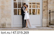 Happy newlyweds embracing each other by the white entrance door with windows. Стоковое фото, фотограф David Kashakhi / Фотобанк Лори