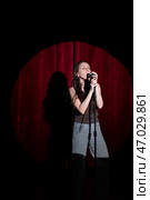 Young woman in jeans and a T-shirt standing behind a microphone on stage and singing. Performing a monologue on stage. Стоковое фото, фотограф Кашапова Эльвира / Фотобанк Лори