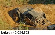 A muddy off-road vehicle designed for extreme off-roading partially peeks out of a deep puddle. The rear part of the vehicle is in water. There is a steep dirt slope in front of it. Стоковое фото, фотограф Воловодов Владимир / Фотобанк Лори