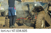 A dirty SUV chassis, where suspension parts, coiled springs and axles can be seen among the steam and mud. A man in dark clothes and blue shorts stands nearby and unhooks the winch cable. Стоковое фото, фотограф Воловодов Владимир / Фотобанк Лори