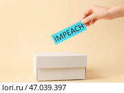 Рука кладет бумагу с текстом IMPEACH в ящик для голосования на цветном фоне. Стоковое фото, фотограф Pixel_shot / Фотобанк Лори