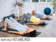 Elderly woman in company of hatha yoga lovers performs bridge pose, setu bandha sarvangasana. Стоковое фото, фотограф Яков Филимонов / Фотобанк Лори