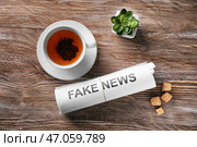 Рулон бумаг с фразой «Фальшивые новости» и чашкой чая на деревянном столе. Стоковое фото, фотограф Pixel_shot / Фотобанк Лори