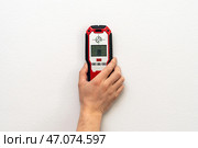 Man using stud finder to locate framing studs located behind the walling surface. Using a wall scanner to identify hidden electrical wiring. Space for text. (2022 год). Редакционное фото, фотограф Луиза Налимова / Фотобанк Лори