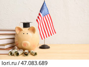 Копилка с деньгами, книги и флаг США на столе возле светлой стены. Концепция студенческого займа. Стоковое фото, фотограф Pixel_shot / Фотобанк Лори