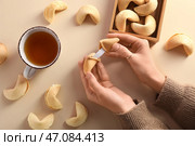 Женские руки с разломанным печеньем с предсказанием и чашкой чая на бежевом фоне. Стоковое фото, фотограф Pixel_shot / Фотобанк Лори