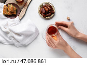 Женские руки с стаканом турецкого чая, сушеными финиками и вкусной баклавой на белом фоне. Стоковое фото, фотограф Pixel_shot / Фотобанк Лори
