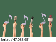 Женские руки держат микрофоны с нотными листами на темно-зеленом фоне. Стоковое фото, фотограф Pixel_shot / Фотобанк Лори