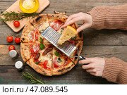 Руки женщины натирают сыр для вкусной пиццы на деревянной поверхности, вид сверху. Стоковое фото, фотограф Pixel_shot / Фотобанк Лори