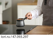 Женщина держит в руках джезву с горячим сваренным кофе возле плиты на кухне. Стоковое фото, фотограф Pixel_shot / Фотобанк Лори