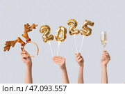 Женские руки с фигурками 2025 из воздушных шаров из фольги, бокал шампанского и ободок с рогами на белом фоне. Стоковое фото, фотограф Pixel_shot / Фотобанк Лори