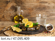 Тарелка с вкусными долмой (фаршированные виноградные листья), лимоном, специями и маслом на деревянном фоне. Стоковое фото, фотограф Pixel_shot / Фотобанк Лори