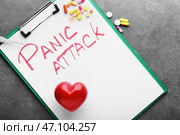 Буфер обмена с текстом ПАНИЧЕСКАЯ АТАКА, сердце и разбросанные таблетки на сером фоне. Стоковое фото, фотограф Pixel_shot / Фотобанк Лори