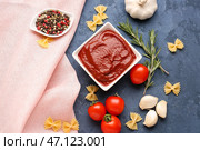 Композиция с миской вкусной томатной пасты, сырой пастой фарфалле и розмарином на сером фоне. Стоковое фото, фотограф Pixel_shot / Фотобанк Лори