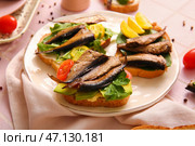 Тарелка вкусных бутербродов с консервированными копчеными шпротами на столе. Стоковое фото, фотограф Pixel_shot / Фотобанк Лори
