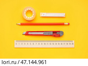 Универсальный нож с клейкой лентой, лезвиями, карандашом и линейкой на желтом фоне. Стоковое фото, фотограф Pixel_shot / Фотобанк Лори