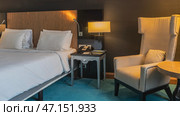 Bedroom interior. The double bed is covered with white sheets. Pillows at the headboard. There is a telephone and writing materials on the bedside table. The wall sconces are lit. A soft armchair. Стоковое фото, фотограф Вера Ивановна Кубарева / Фотобанк Лори