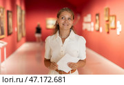 Young girl holding an information booklet looks at paintings in an art exhibition in museum. Стоковое фото, фотограф Яков Филимонов / Фотобанк Лори