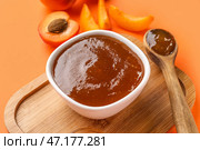 Деревянная доска с миской и ложкой сладкого абрикосового джема на оранжевом фоне. Стоковое фото, фотограф Pixel_shot / Фотобанк Лори