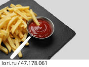 Черная шиферная доска с золотистыми картофельными палочками и кетчупом на сером фоне, крупным планом. Стоковое фото, фотограф Pixel_shot / Фотобанк Лори