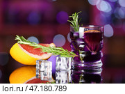 Стакан с фиолетовым джином и тоником с кубиками льда, грейпфрутом и розмарином на столе в баре на фоне размытого заднего плана. Стоковое фото, фотограф Pixel_shot / Фотобанк Лори