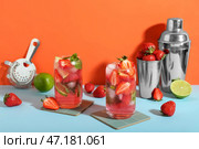 Стаканы с свежим клубничным мохито с шейкерами, ситом и ингредиентами на голубом столе у оранжевой стены. Стоковое фото, фотограф Pixel_shot / Фотобанк Лори