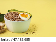 Тарелка вкусной гречневой каши с яйцом всмятку и свежим огурцом на желтом фоне. Стоковое фото, фотограф Pixel_shot / Фотобанк Лори