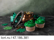 Вкусные кексы на День Святого Патрика, горшочек с монетами и подкова на черном гранж-столе. Стоковое фото, фотограф Pixel_shot / Фотобанк Лори