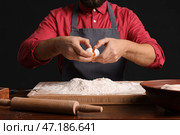 Мужчина-пекарь разбивает яйцо для теста за столом на темном фоне, крупным планом. Стоковое фото, фотограф Pixel_shot / Фотобанк Лори