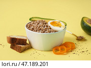 Тарелка вкусной гречневой каши с яйцом всмятку, свежими овощами и хлебом на желтом фоне. Стоковое фото, фотограф Pixel_shot / Фотобанк Лори